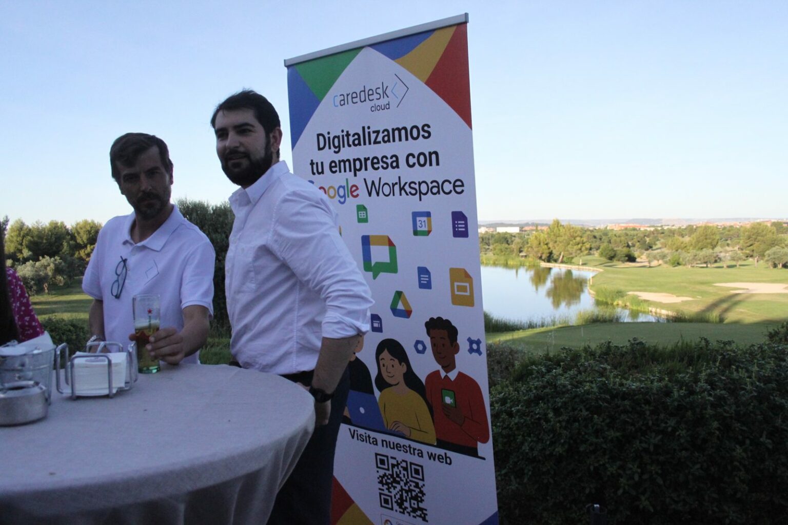 Dos asistentes junto al roll-up Digitalizamos tu empresa con Google Workspace, con el campo de golf al atardecer de fondo